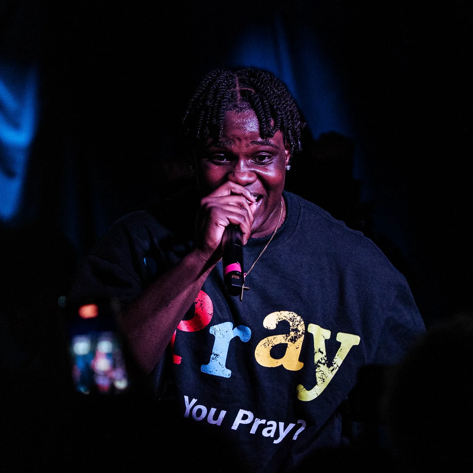 efosa! on stage with a microphone, lit blue, wearing a shirt that asks: You Pray?